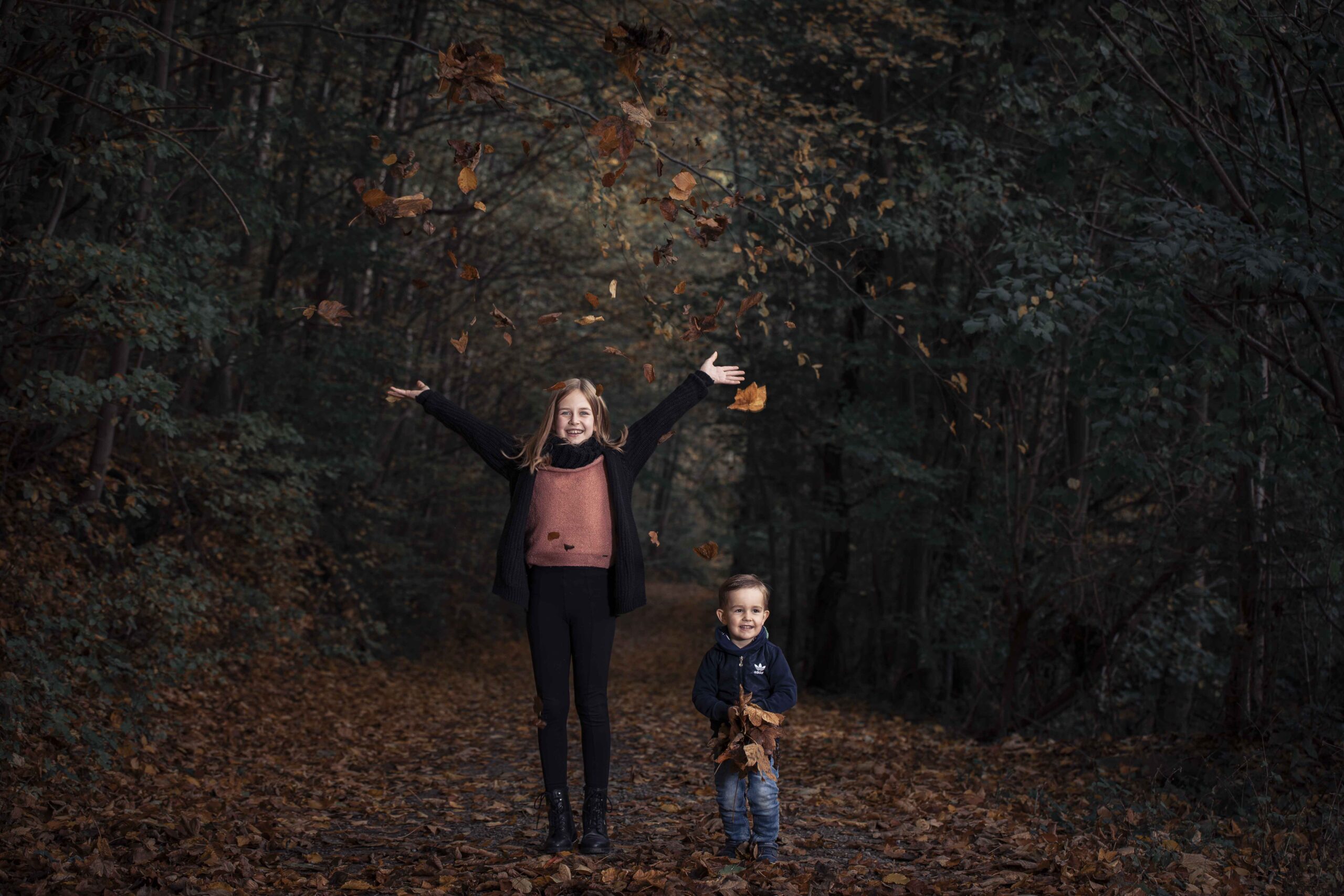 Zwei Kinder werfen bei einem Familienshooting Herbstlaub in die Luft