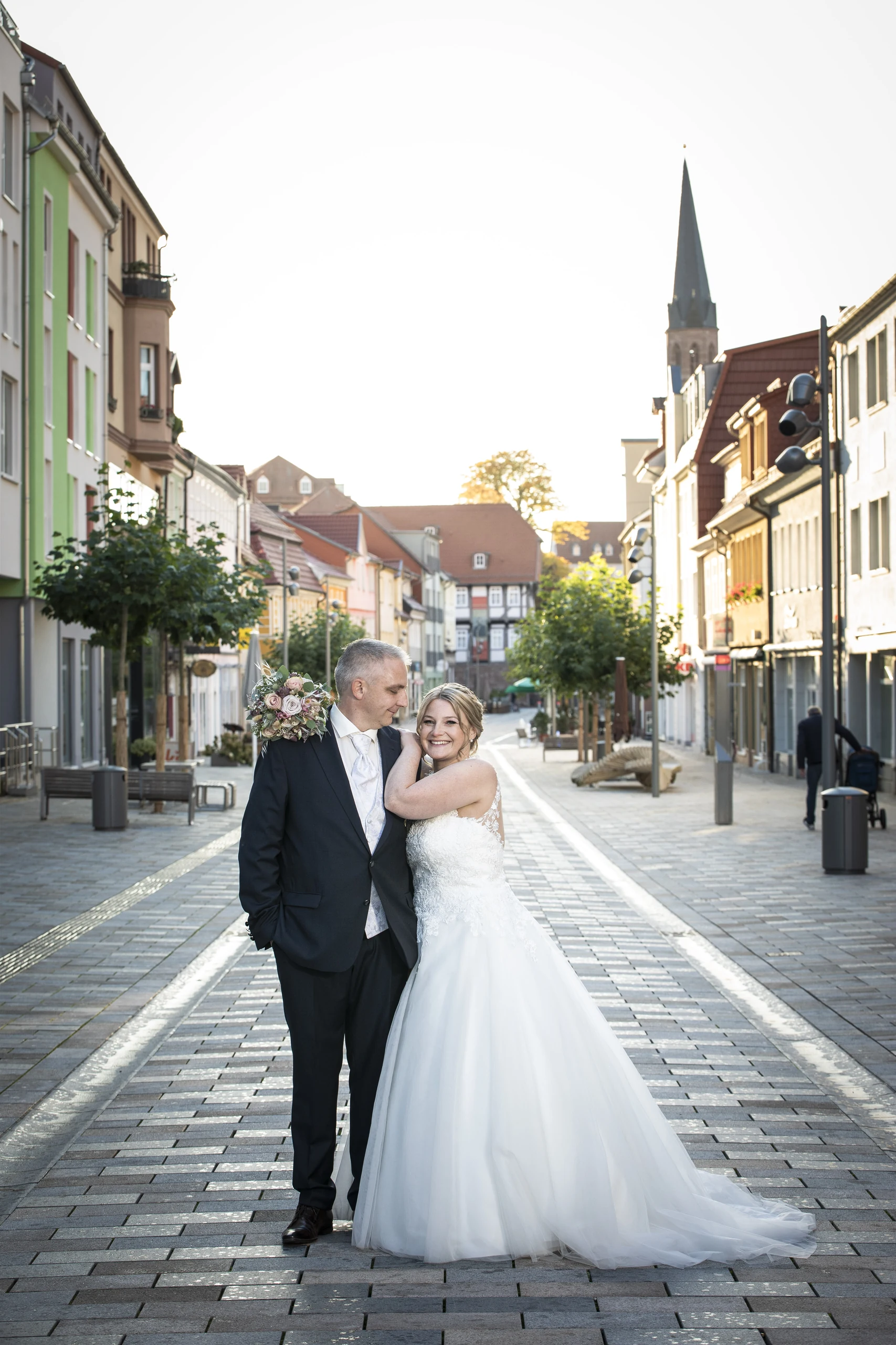 Brautpaar auf einer Straße in Heilbad Heiligenstadt mit Kirchturm im Hintergrund.