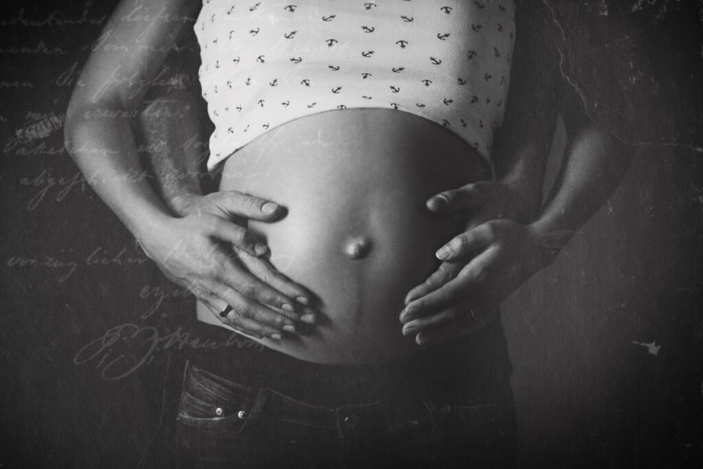Hände auf einem Babybauch bei einer Schwarz-Weiß-Aufnahme.