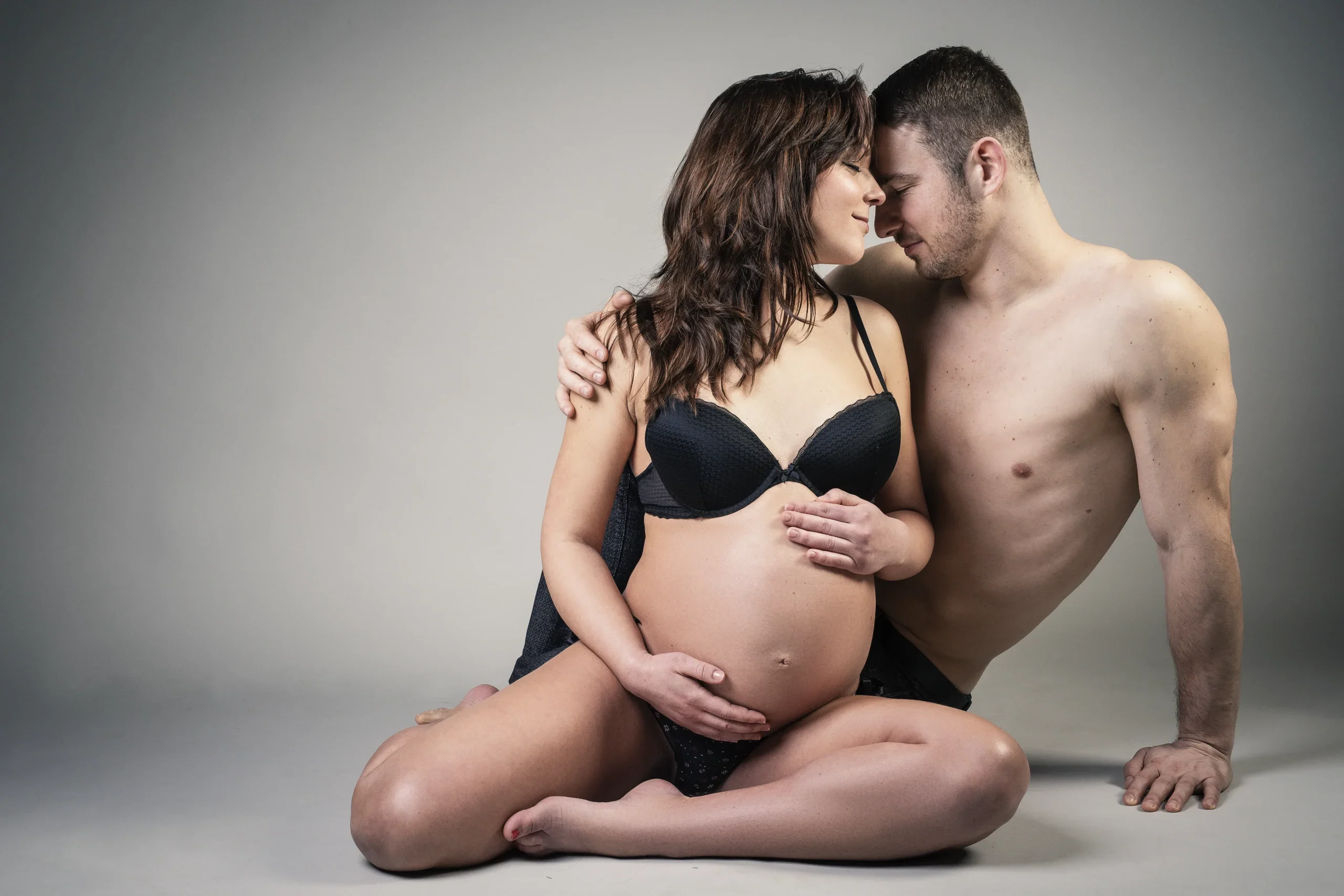 Werdende Eltern sitzen bei einem Babybauchshooting im Studio Stirn an Stirn.