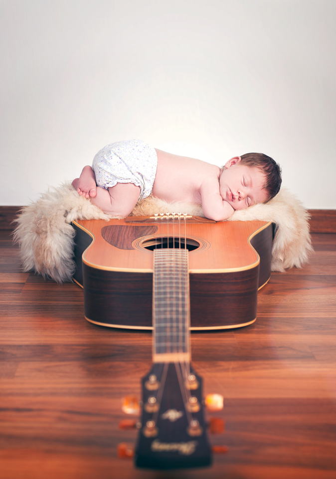 Schlafendes Baby liegt auf einer Akustikgitarre bei einem Newbornshooting