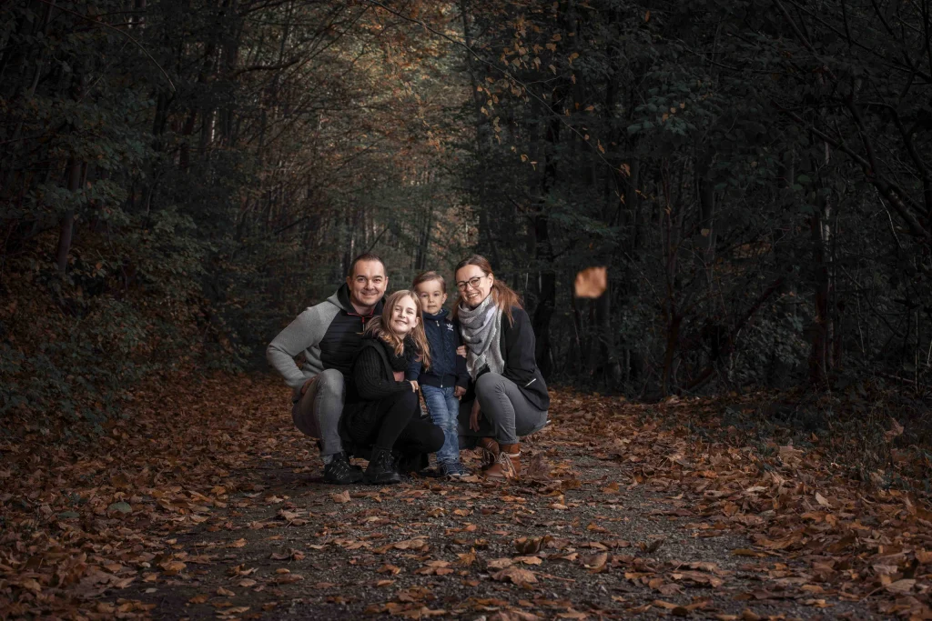 Vierköpfige Familie zwischen fallenden Herbstblättern im Wald.