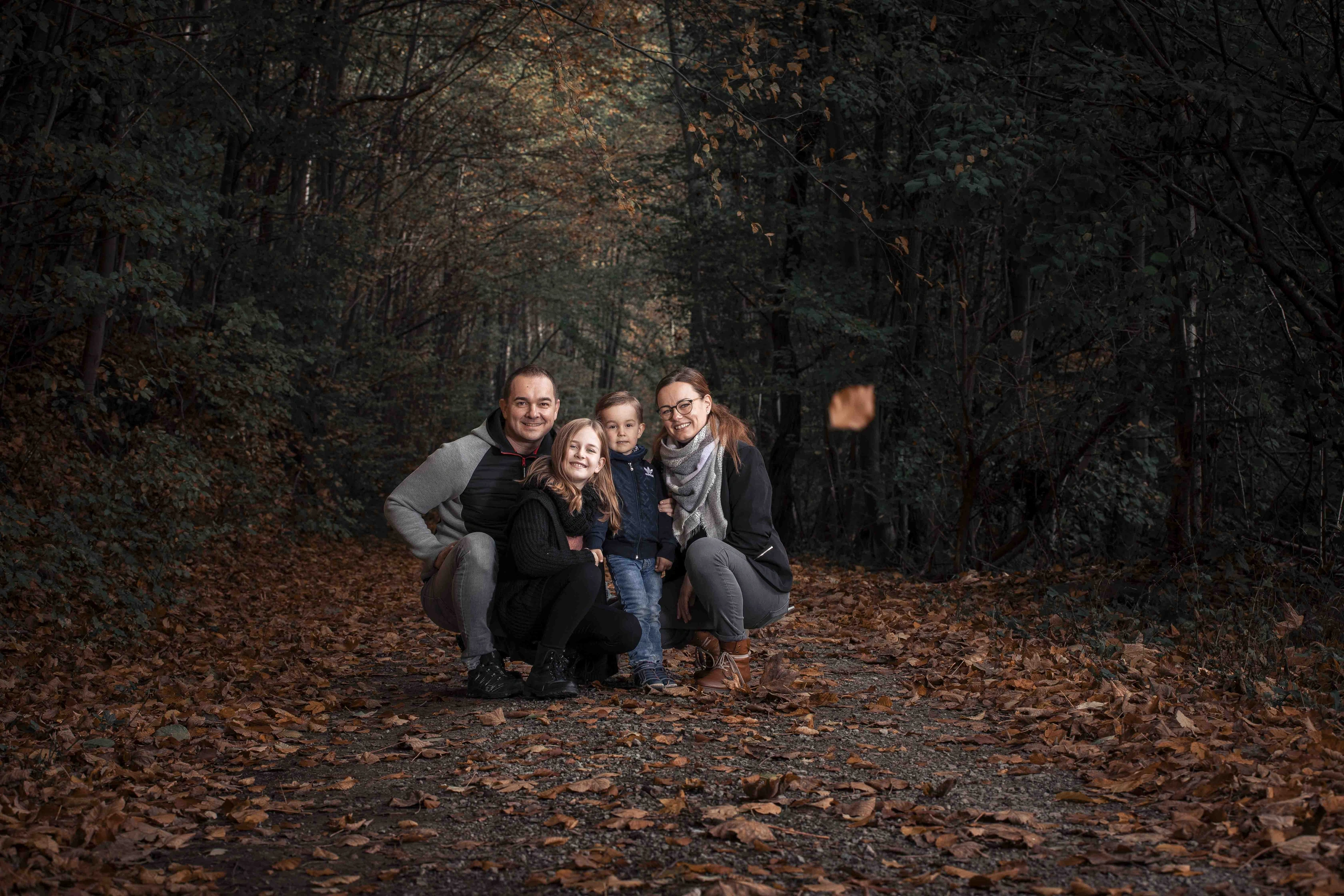 Vierköpfige Familie zwischen fallenden Herbstblättern im Wald.