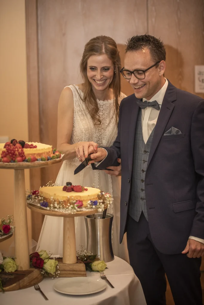 Brautpaar schneidet lachend die Hochzeitstorte auf der Burgruine Hardenberg in Nörten-Hardenberg an.