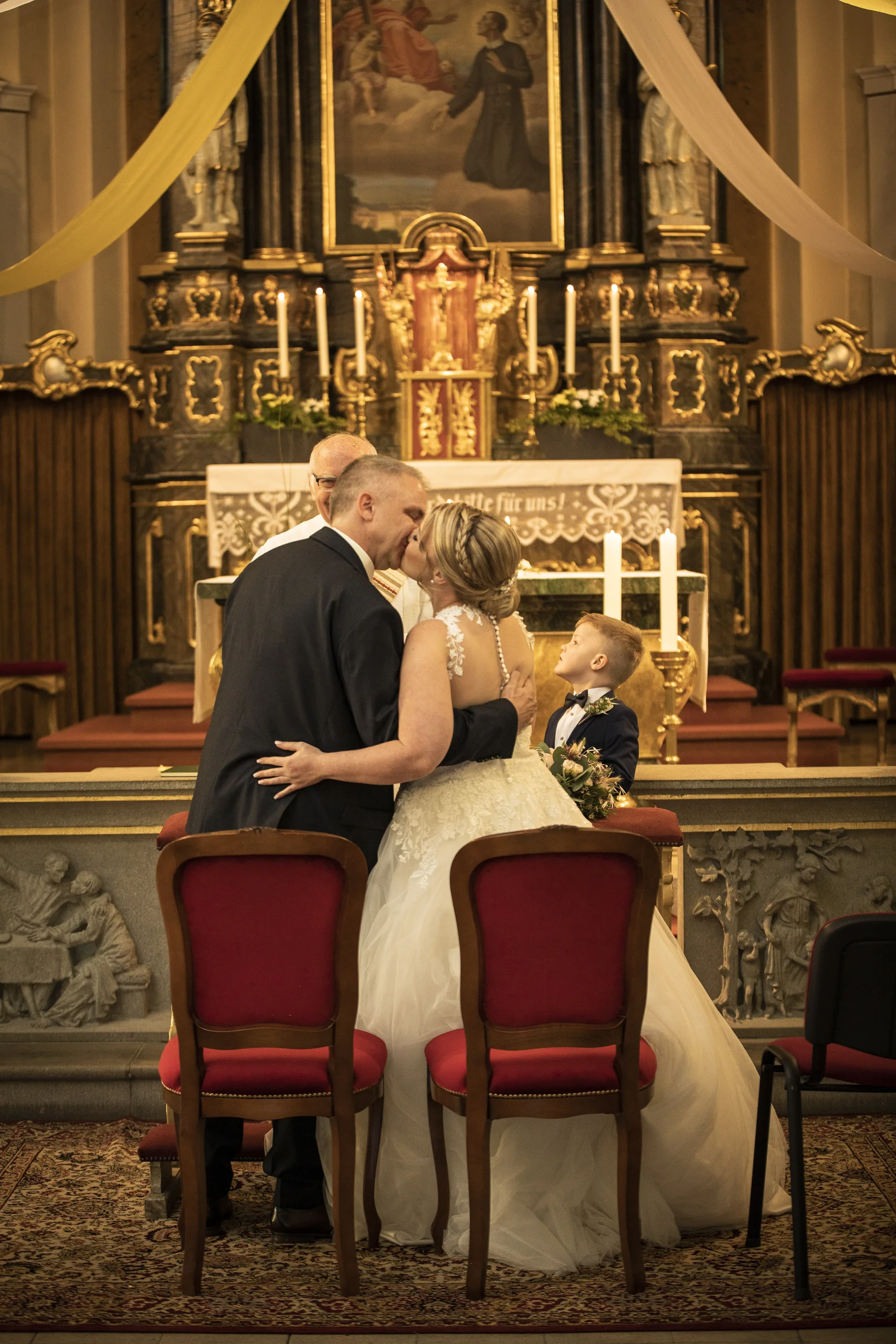 Brautpaar küsst sich hinter roten Trauungsstühlen in der Pfarrkirche St. Gerhard in Heilbad Heiligenstadt.
