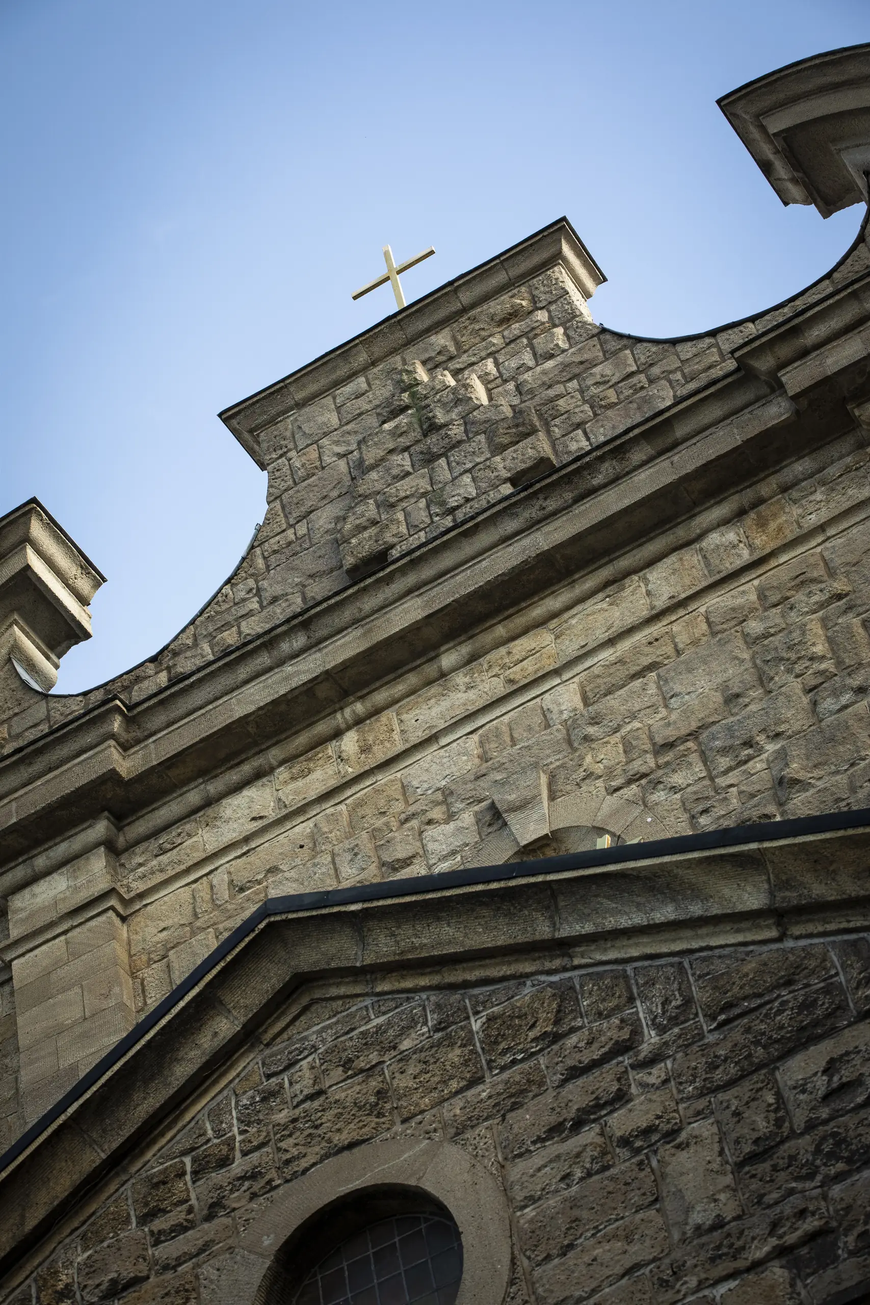 Steinerne Fassade der Pfarrkirche St. Gerhard in Heilbad Heiligenstadt mit Kreuz von unten.