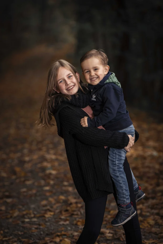 Mädchen trägt einen Jungen bei einem Kinderfoto im Herbstwald.