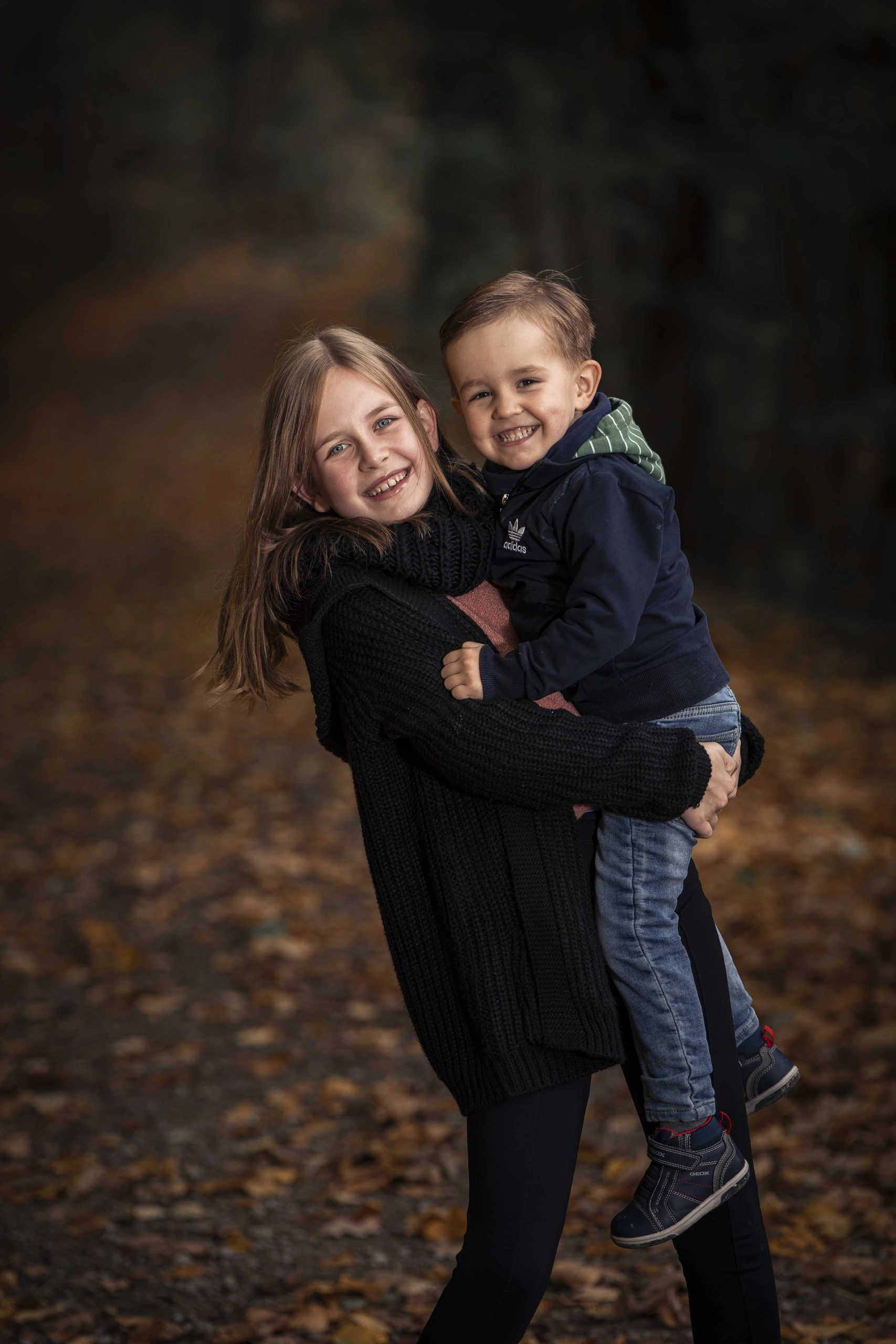 Mädchen trägt einen Jungen bei einem Kinderfoto im Herbstwald.