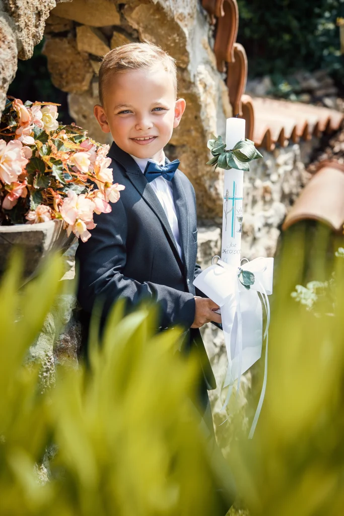 Junge mit Kommunionkerze und Blumen vor einer Steinmauer in Brehme