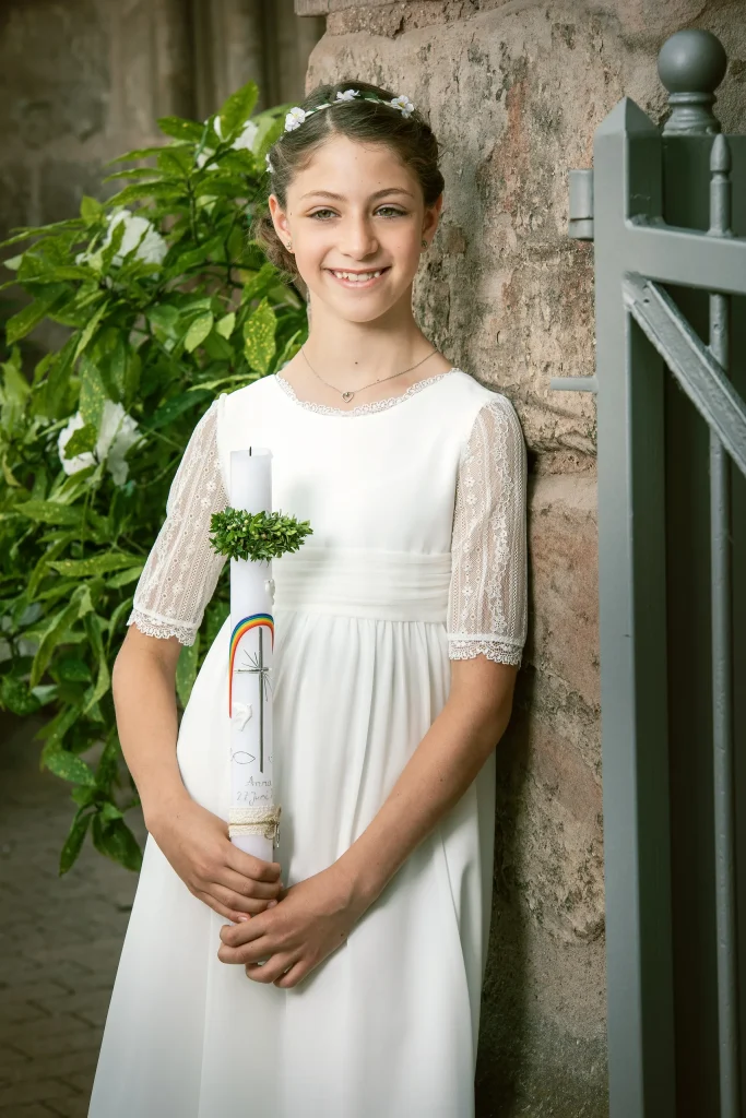 Lachendes Mädchen mit Kommunionkerze neben einem Eisentor in Heilbad Heiligenstadt