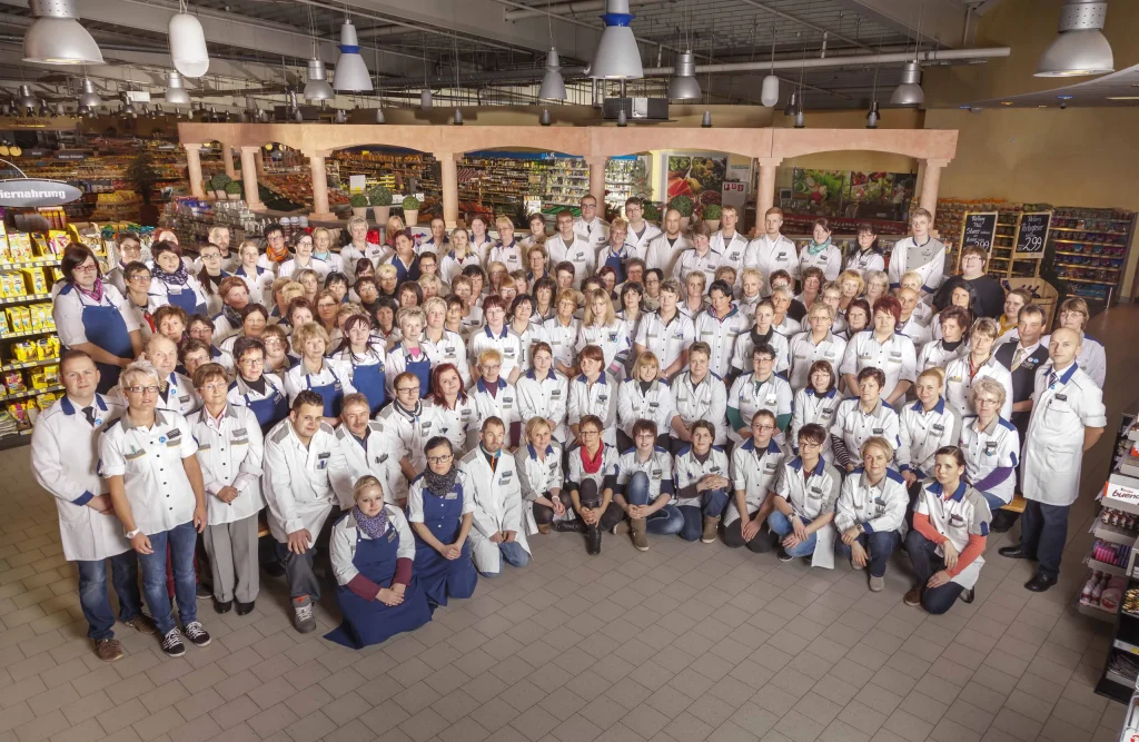 Das Team von Edeka Gotthardt steht und kniet in mehreren Reihen für ein Gruppenfoto im Verkaufsraum.