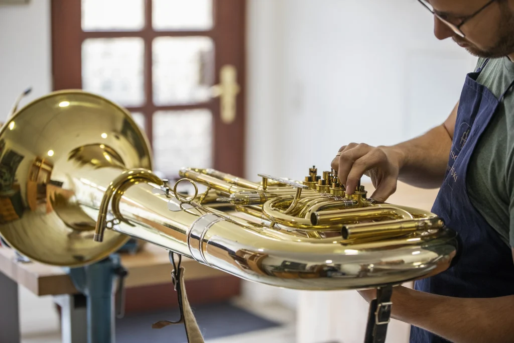Ein Instrumentenbauer arbeitet an der Ventilmechanik einer goldfarbenen Tuba in seiner Werkstatt.