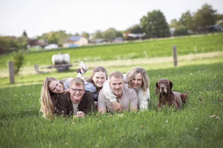 Familie liegt nebeneinander im Gras und schaut in die Kamera.