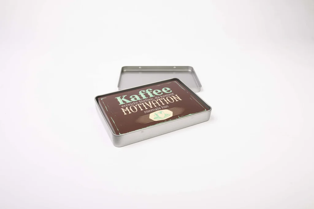 Geöffnete silberne Dose mit einer braunen Karte mit Kaffeespruch auf weißem Hintergrund.