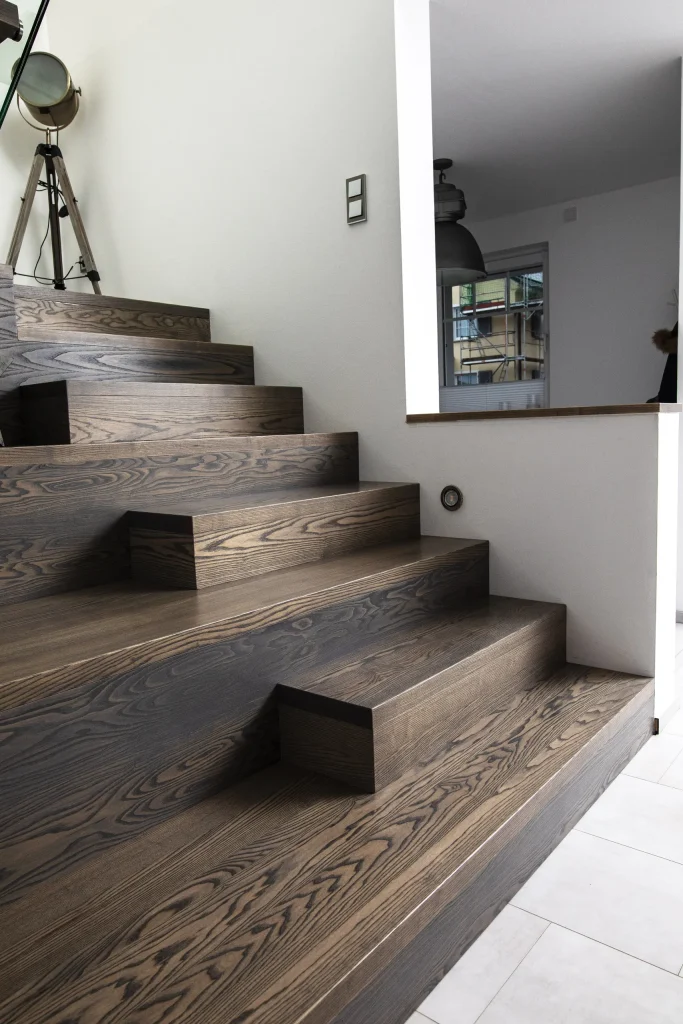 Breite Treppe aus dunkel gemasertem Holz mit versetzt angeordneten Stufen in einem hellen Wohnraum.