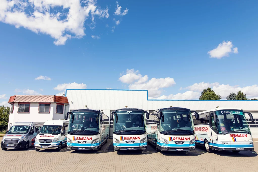 Vier Reisebusse und zwei Kleinbusse von Reimann Reisen stehen nebeneinander auf dem Betriebshof.